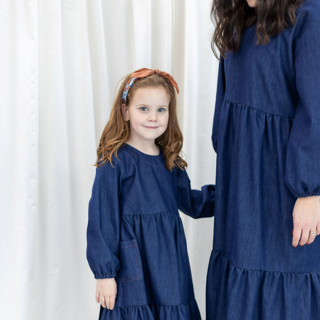 Ladies and girls matching blue denim dresses.  Both dresses have gathere tiered skirts, long puff sleeves and are reversable