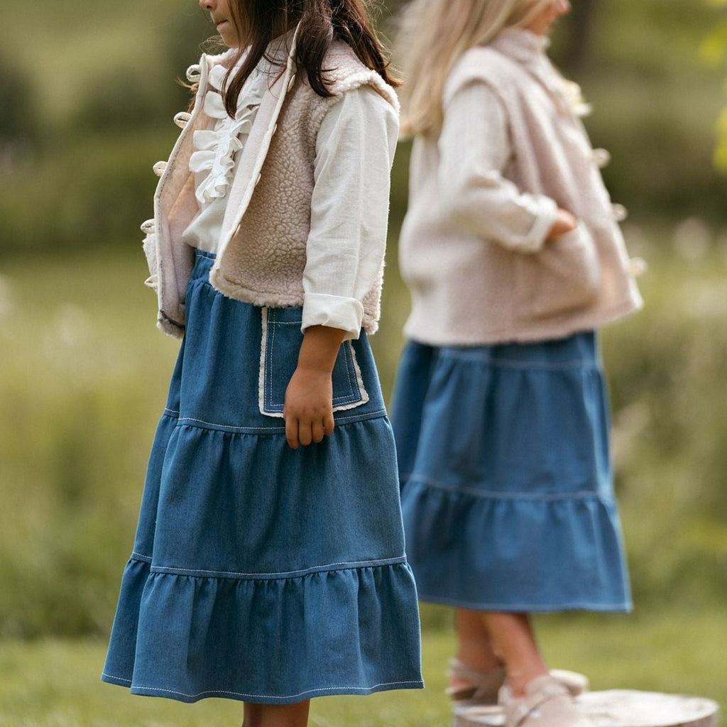 Made from beautifully soft recycled blue denim, the girls skirt is an all round piece.  Made with an adjustable elastic waistband to get a great fit and an oversized pocket edged with cotton scallop trim.  Worn with the unisex offwhite ruffle shirt and unisex beige faux fur gilet beige 